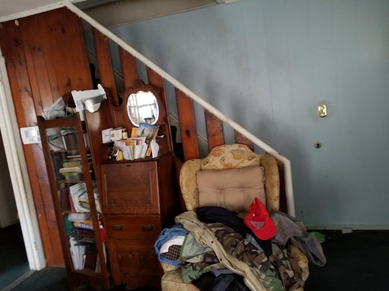 Living room stairs before the renovation with piled up clothes on the couch