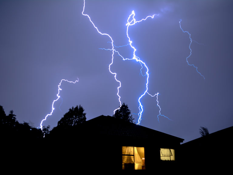 A dark house with a flash of lightning and a light inside on it