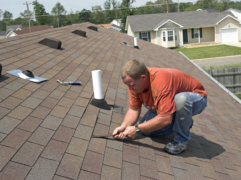 A man using a chisel on an asphalt roof